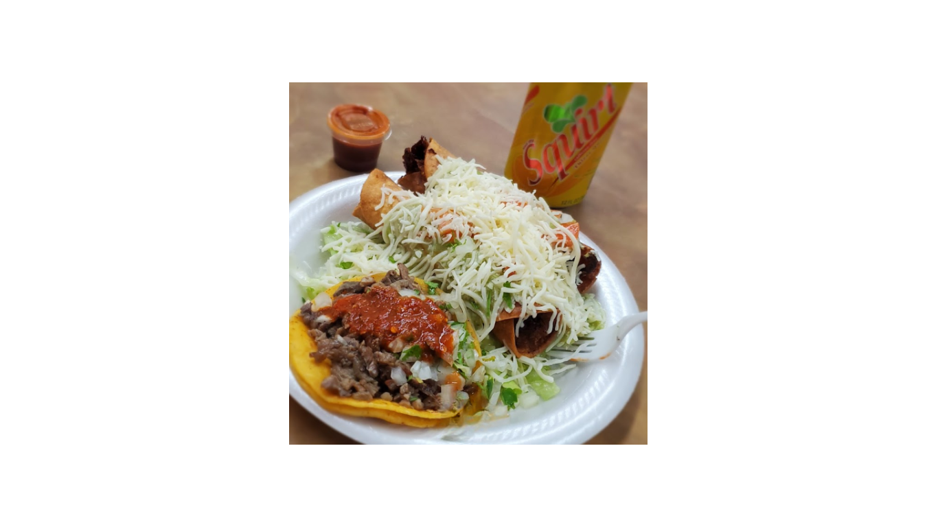 Carne asada tacos and flautas topped with fresh cheese and salsa on a plate at Taqueria Los Compadres, with a Jarritos soda in the background.