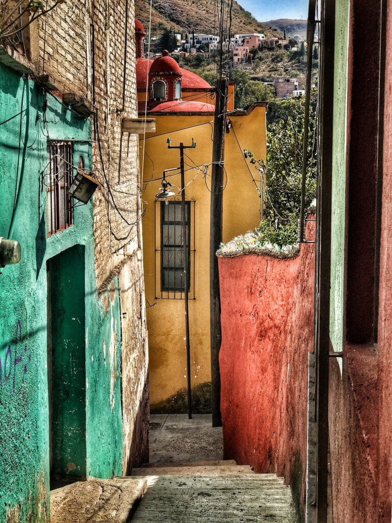 Narrow colorful street in Mexico with vibrant green, yellow, and red buildings, symbolizing the rich cultural ambiance of Taqueria Los Compadres.